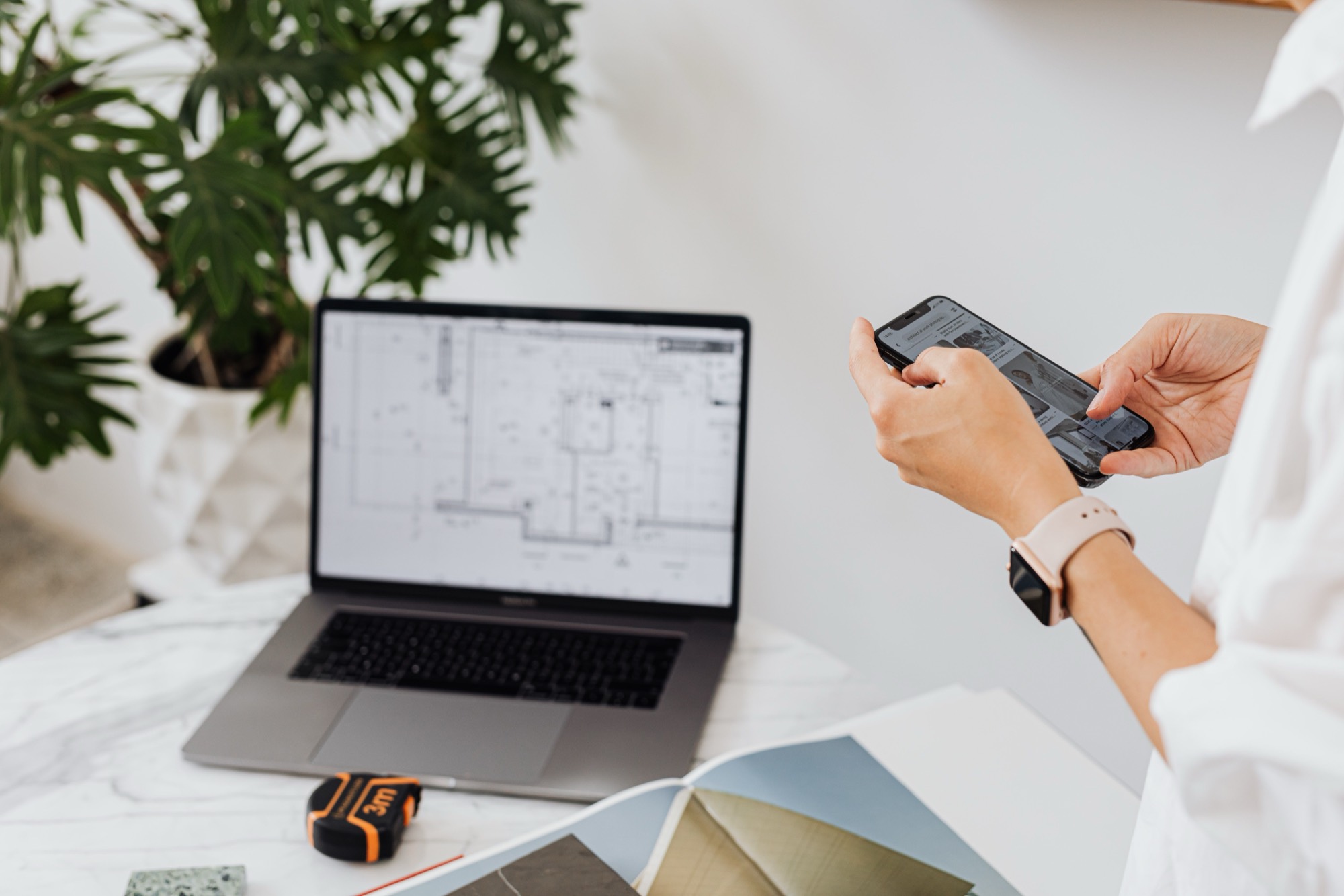 Construction professional reviewing building drawings on a laptop while using a phone